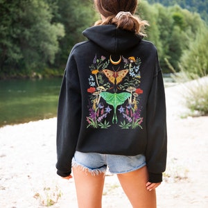 May include: Black hooded sweatshirt with a colorful floral and butterfly design on the back. The design features moths, mushrooms, and flowers.