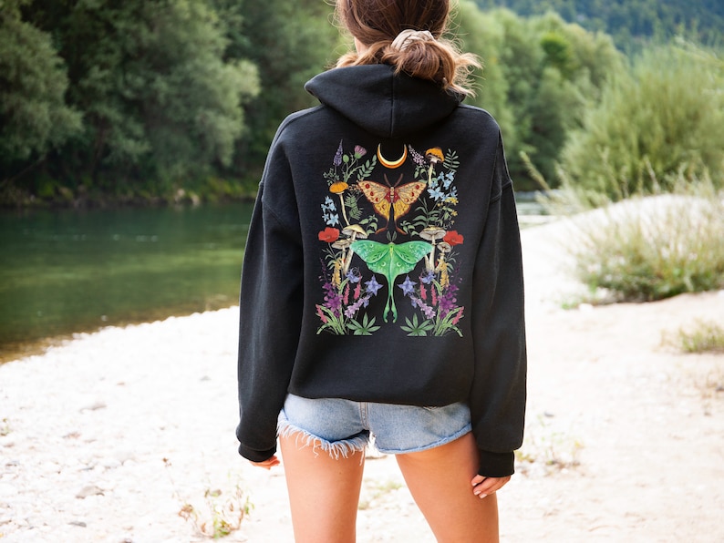 May include: Black hooded sweatshirt with a colorful floral and butterfly design on the back. The design features moths, mushrooms, and flowers.