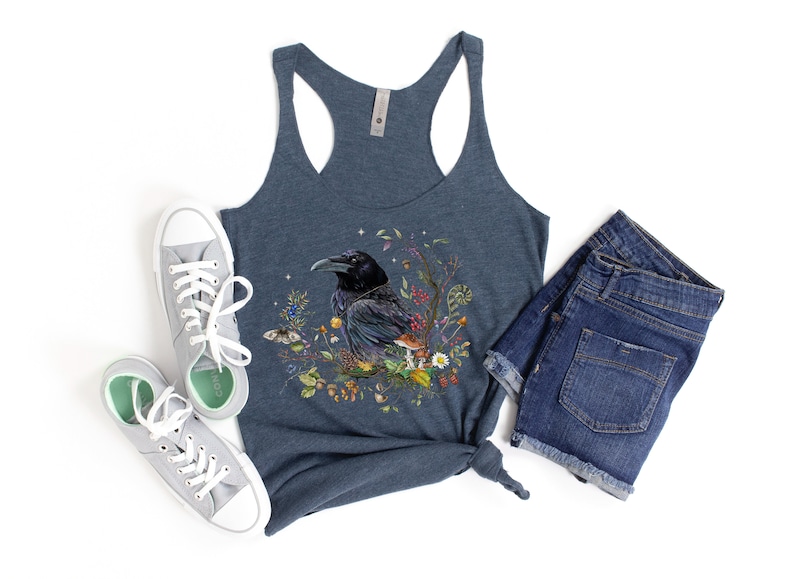 K&ouml;nnte beinhalten: Ein dunkelblaues Tanktop mit einem Aufdruck eines schwarzen Rabens, umgeben von Blumen und Pilzen. Das Tanktop ist aus einem weichen, bequemen Material gefertigt.