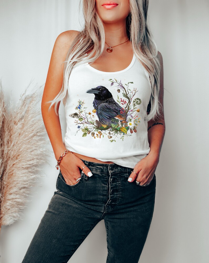 K&ouml;nnte beinhalten: Ein wei&szlig;es Tanktop mit einer schwarzen Kr&auml;he Illustration, umgeben von Blumen und Bl&auml;ttern. Die Kr&auml;he sitzt auf einem Ast mit Beeren und Eicheln.