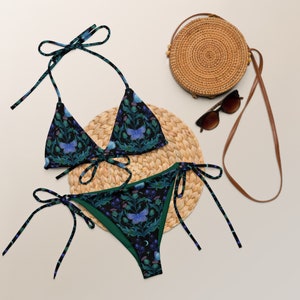 May include: A black and green bikini with a floral and butterfly print. The bikini top is a triangle style with adjustable straps. The bikini bottom is a high-cut style with ties on the sides.
