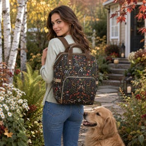 May include: A black backpack featuring a detailed print of mushrooms, snakes, foxes, and celestial motifs like moons and stars. The bag includes brown straps, a top handle, and a front zippered pocket, constructed with a structured rectangular shape.
