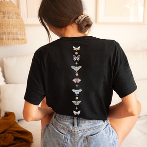 May include: A black t-shirt with a vertical row of colorful butterflies and gold stars printed on the back.