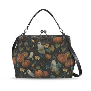 May include: A black handbag with a Halloween-themed pattern featuring orange pumpkins, white ghosts, and yellow flowers. The bag has a black handle and a detachable shoulder strap. The clasp is silver-toned.