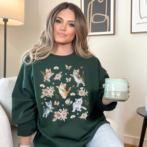 May include: A dark green sweatshirt with a print of kittens and butterflies. The sweatshirt has a crew neck and long sleeves.