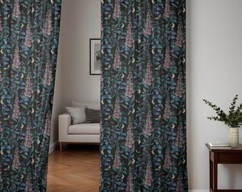 May include: Two black sheer curtains with a floral pattern featuring pink and blue flowers, leaves, and crescent moons. The curtains are hanging in a room with a white couch and a wooden floor.