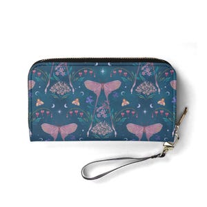 Op de afbeelding: Tealkleurige portemonnee met ritssluiting en een herhalend patroon van roze motten, bloemen en hemelse elementen. De portemonnee heeft een polsbandje en een goudkleurige ritstrekker. Het ontwerp is grillig en geïnspireerd door de natuur.