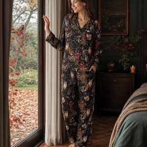 Puede incluir: Un conjunto de pijama negro de camisa de manga larga con botones y pantalón a juego, con un estampado repetitivo de zorros, búhos, setas y elementos florales rojos. El conjunto presenta un cuello con muescas y un corte recto y relajado.