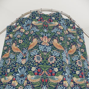 Puede incluir: Una cortina de ducha con un patr&oacute;n repetitivo de p&aacute;jaros estilizados, flores y hojas. El patr&oacute;n es en tonos de azul, verde, rojo y amarillo sobre un fondo azul oscuro.