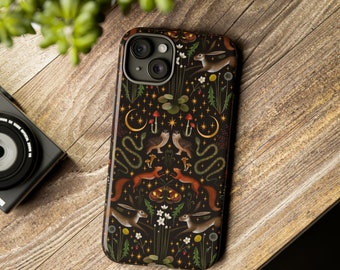 May include: A black phone case with a whimsical forest design. The case features illustrations of hares, squirrels, owls, mushrooms, and crescent moons against a backdrop of stars and foliage. The case is on a wooden surface.