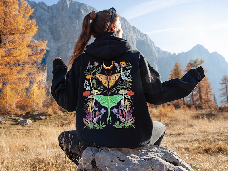 May include: A black hoodie with a colorful embroidered design featuring moths, mushrooms, and flowers. The design is centered on the back of the hoodie.