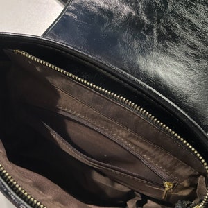 May include: Black leather handbag with a zippered pocket inside. The bag has a gold zipper and a brown lining.