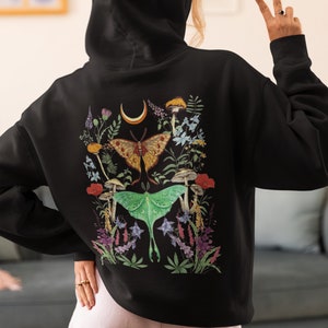 May include: Black hooded sweatshirt with a colorful print of moths, mushrooms, and flowers on the back.