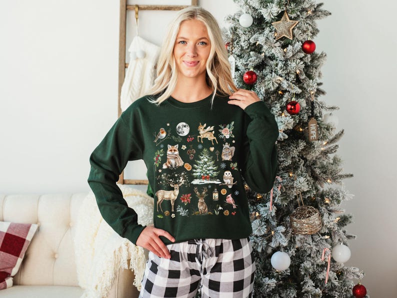 May include: A green Christmas sweater with a woodland scene featuring animals, plants, and a small Christmas tree. The sweater has a crew neck and long sleeves.
