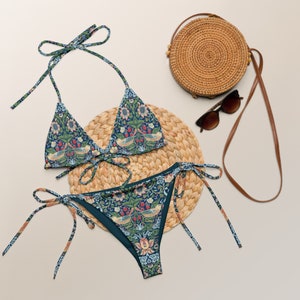 May include: A blue and green floral print bikini with a triangle top and a high-cut bottom. The bikini is on a woven straw mat with a round straw bag and sunglasses.