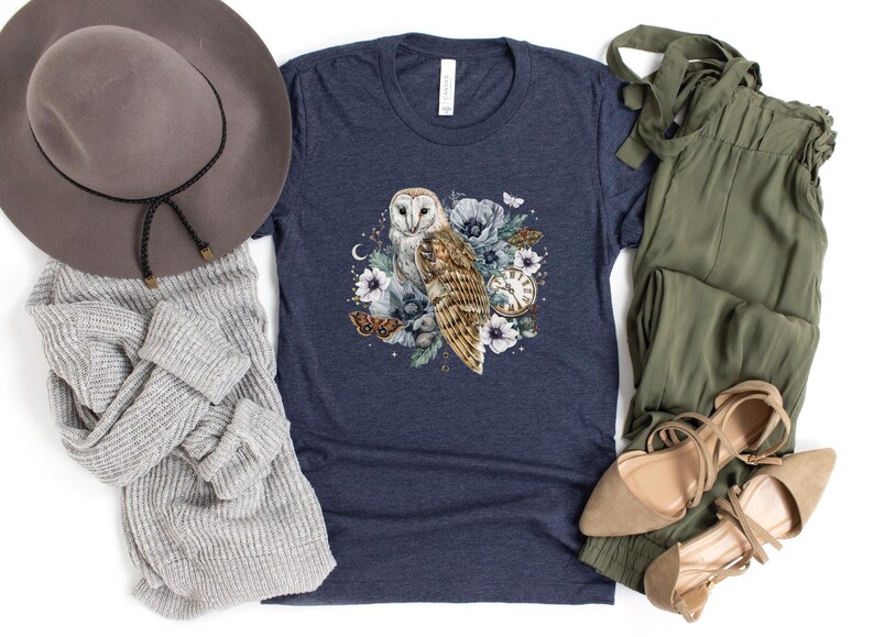 May include: A navy blue t-shirt with a white barn owl illustration surrounded by flowers, butterflies, and a vintage pocket watch. The owl has a white face and brown and white feathers.