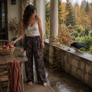 May include: A pair of loose-fitting trousers featuring a dark background with a vibrant red poppy floral pattern, paired with a simple cream-colored spaghetti strap tank top. The trousers have a relaxed, wide-leg silhouette and an elasticized waistband.