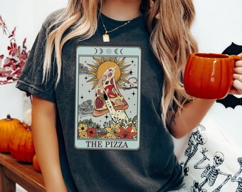 May include: A dark gray t-shirt with a vintage tarot card design featuring a hand holding a slice of pizza. The card is titled "The Pizza" and has a sun, moon, and stars in the background.