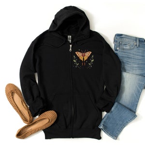 May include: Black zip-up hoodie with a colorful butterfly graphic on the front. The butterfly has yellow, orange, and red wings with black outlines. The hoodie has a hood and a zipper closure.