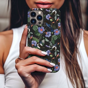 May include: A black phone case with a floral design featuring blue and white flowers, green leaves, and black birds. The case has a camera lens cutout and a black background.