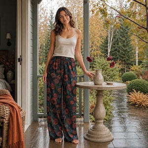May include: A beige sleeveless tank top paired with wide-leg trousers featuring a dark green background and a vibrant red poppy floral pattern. The trousers have an elasticized waistband and a loose, flowing fit that reaches the floor.
