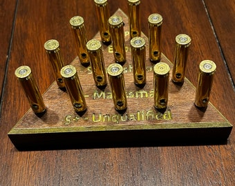 May include: A wooden triangle-shaped display stand with 15 brass bullet casings arranged in a triangular pattern. The stand has engraved text that reads "5+ - Unqualified" and "- Marksman". The bullets are gold-colored and stand upright.