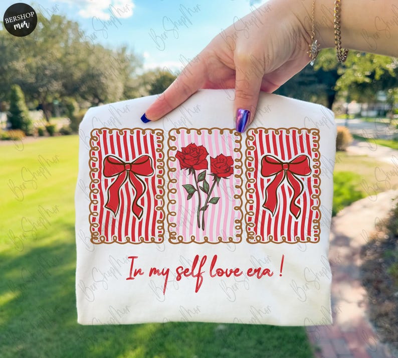 May include: A white t-shirt featuring three framed designs. The designs include red bows on red and white striped backgrounds and red roses on a pink and white striped background. The text "In my self love era!" is printed below.