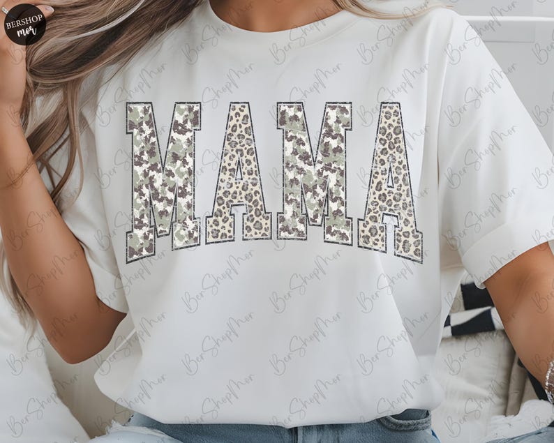 May include: White t-shirt with the word "MAMA" in large, block letters. The letters have a camouflage and leopard print design. The shirt is a casual style.
