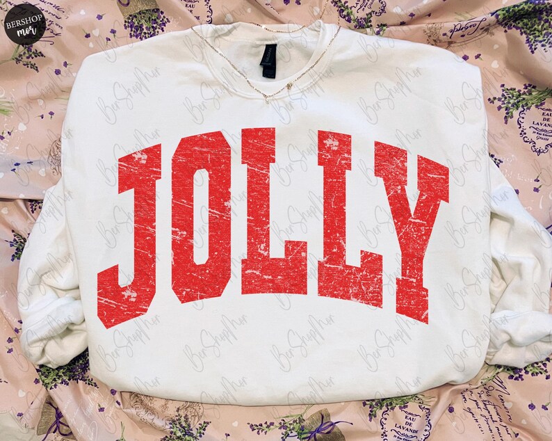 May include: White sweatshirt with the word "JOLLY" in distressed red lettering across the front. The sweatshirt has a V-neck and long sleeves. The overall style is casual and festive, perfect for the holiday season.