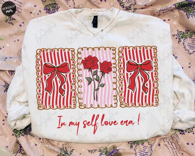 May include: White sweatshirt with a graphic design featuring red roses, red bows, and vertical red stripes. The text "In my self love era!" is written in red script below the design. The sweatshirt has a V-neck.