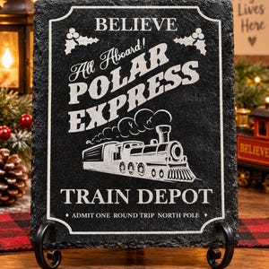 May include: A rectangular black slate sign with a rough, chiseled edge, featuring white engraved text that reads BELIEVE, All Aboard! POLAR EXPRESS, and TRAIN DEPOT, along with a steam locomotive illustration and holly accents.