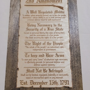 May include: A wooden sign with the text "2nd Amendment" in a decorative font. The text includes the full text of the Second Amendment to the United States Constitution, which reads: "A well regulated Militia, being necessary to the security of a free State, the right of the people to keep and bear Arms, shall not be infringed." The sign also includes the date "Est. December 15th, 1791".