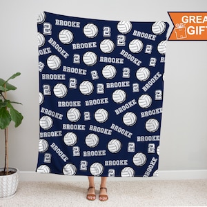 Op de afbeelding: Een navyblauwe fleece deken met een witte volleybal en de naam "Brooke" die over het hele ontwerp wordt herhaald. Het nummer "2" wordt ook over het hele ontwerp herhaald.