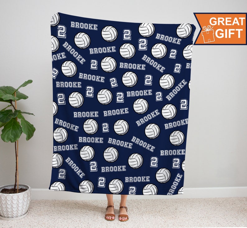 Op de afbeelding: Een navyblauwe fleece deken met een witte volleybal en de naam "Brooke" die over het hele ontwerp wordt herhaald. Het nummer "2" wordt ook over het hele ontwerp herhaald.