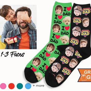 May include: Two pairs of custom socks. One pair is green with the text "I ❤️ YOU DAD" and faces. The other pair is black with "SUPER DAD" text and faces. The image also shows a gift box and a person.