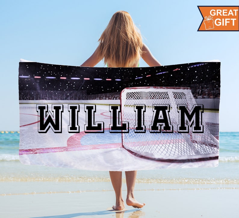 May include: A personalized beach towel featuring a hockey rink design with the name "WILLIAM" in bold, black and white lettering. The towel includes a hockey net and a stadium background. The words "GREAT GIFT" are in the upper right corner.