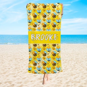 May include: A yellow beach towel with a pattern of cartoon bees and honeycombs. The towel has the name "BROOKE" printed in white on a yellow stripe.