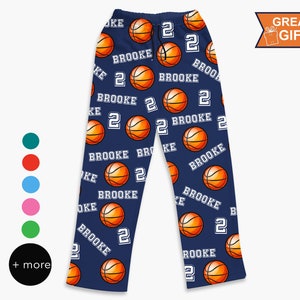May include: Navy blue pajama pants featuring an all-over print of orange basketballs, the name BROOKE in white block letters, and the number 2 in white. The pants have an elastic waistband with a black drawstring and a straight-leg cut.