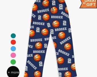Puede incluir: Pantalones de pijama azul marino con un estampado integral de balones de baloncesto naranjas, el nombre BROOKE en letras blancas y el número 2 en blanco. Los pantalones tienen una cintura elástica con cordón negro y corte recto.