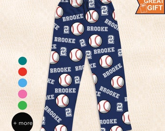 Pode incluir: Calças de pijama azul-marinho com um padrão repetitivo de bolas de basebol brancas com costuras vermelhas, o nome BROOKE em letras brancas e o número 2 em branco. As calças têm uma cintura elástica com um cordão preto.