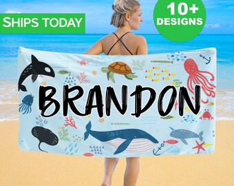 May include: A blue beach towel with a sea life design. The towel features a whale, octopus, sea turtle, fish, and other sea creatures. The name "BRANDON" is printed in black across the towel.