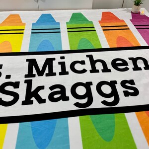 K&ouml;nnte beinhalten: Eine wei&szlig;e Fleece-Decke mit einem bunten Kreidendesign und dem Text "Mrs. Michenni Skaggs" in Schwarz gedruckt.