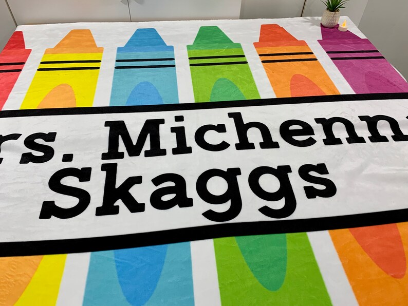 K&ouml;nnte beinhalten: Eine wei&szlig;e Fleece-Decke mit einem bunten Kreidendesign und dem Text "Mrs. Michenni Skaggs" in Schwarz gedruckt.