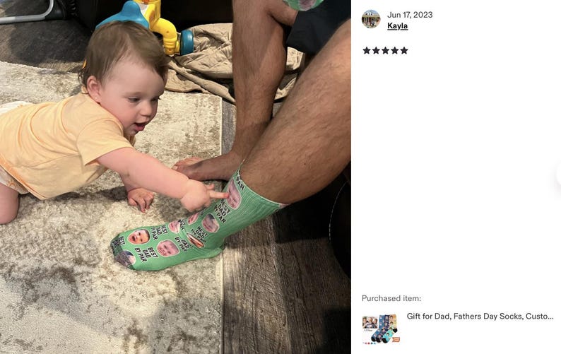 Pode incluir: Uma meia verde clara com fotos e texto personalizados, com um beb&ecirc; apontando para ela. A meia tem v&aacute;rias imagens e o texto "BEST DAD BY FAR". Um beb&ecirc; com uma camisa amarela est&aacute; engatinhando em um tapete.