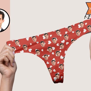 May include: Red thong underwear featuring a repeating pattern of white hearts and a repeated photographic print of a man's face. The garment has a high-cut leg design and a thin waistband. A circular inset shows the original face photo.