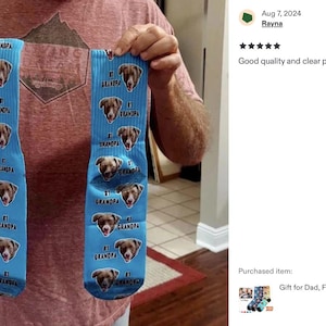 Pode incluir: Um par de meias azul claro com um padr&atilde;o repetido do rosto de um c&atilde;o e as palavras "#1 Grandpa". As meias s&atilde;o levantadas, mostrando o design. As meias s&atilde;o um presente para o Dia dos Pais.