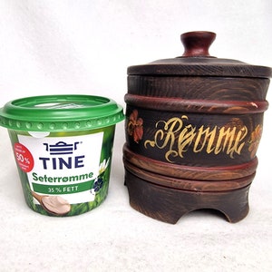 May include: A green plastic container of Tine Seterromme cream cheese with a wooden barrel-shaped container with the word "Rømme" painted on it in gold lettering.