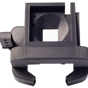 May include: A black 3D printed plastic part with a square opening and a rounded top. The part has a clamp design on the bottom.