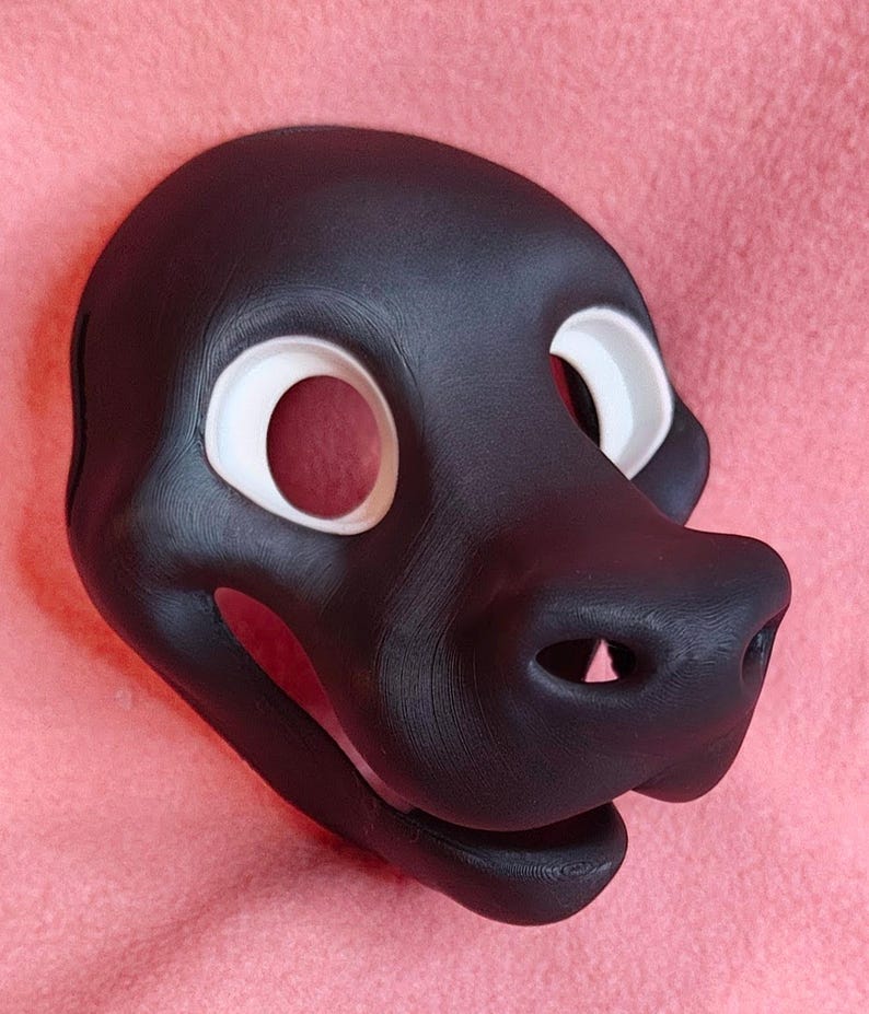 Op de afbeelding: Een zwart dierenmasker met witte oogomrandingen. Het masker heeft een prominente snuit met twee neusgaten en een lachende mond. Waarschijnlijk voor cosplay of kostuums.