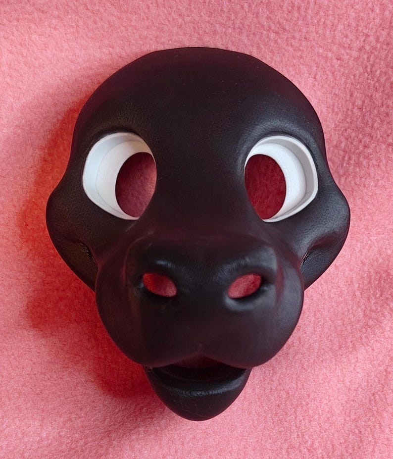 Op de afbeelding: Een zwart dierenmasker met grote, witte oogopeningen en een prominente snuit. Het masker is gemaakt van een glad materiaal en heeft een gedetailleerd ontwerp, inclusief neusgaten en een mond. Het masker is ontworpen om gedragen te worden.
